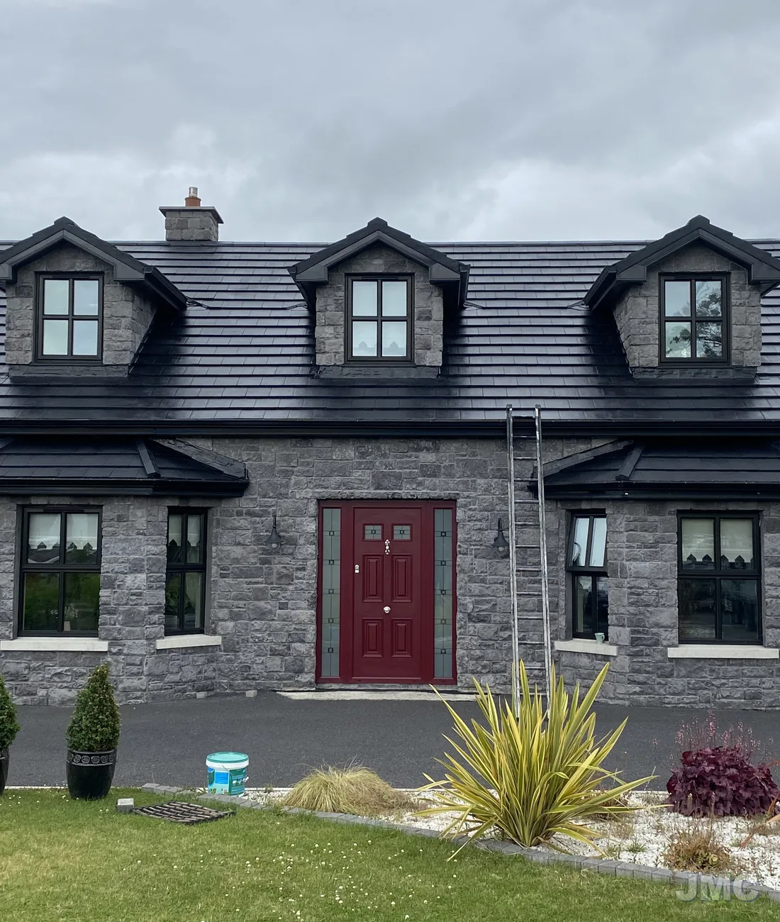 A stone-fronted house with a newly sealed roof and a red door
